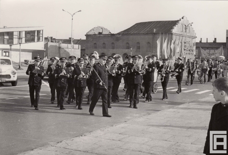 Pochód ludzi, na czele orkiestra w mundurach. Z tyłu widoczna synagoga.