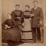 Zdjęcie grupowe u fotografa: trzy kobiety w sukniach i mężczyzna w garniturze.