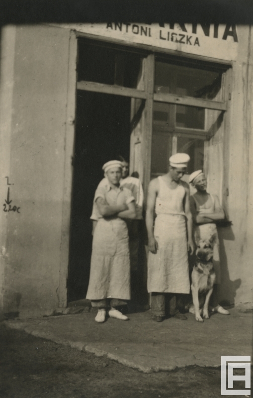 Fotografia przedstawia trzech mężczyzn i kobietę w strojach piekarza, którzy stoją przed drzwiami, obok nich owczarek niemiecki.
