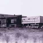 Fotografia przedstawia trzy budynki, na pierwszym planie ceglany, z tyłu oszklony z napisem Tęczowa, w tle blok mieszkalny.