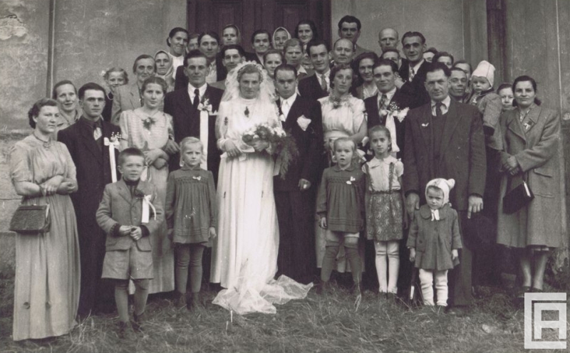 Fotografia przedstawia młodą parę i gości weselnych przed kościołem.