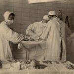 Fotografia przedstawia pielęgniarkę i dwóch lekarzy pochylonych nad stołem operacyjnym. Widoczny stół z narzędziami.