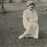 Fotografia przedstawia siedzącą kobietę w stroju służbowym pielęgniarki.