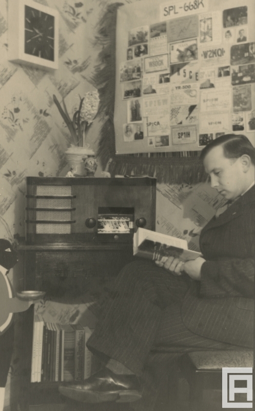 Fotografia przedstawia mężczyznę czytającego książkę. Nad nim wisi tablica z raportami nasłuchowymi.