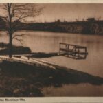 Fotografia przedstawia zbiornik wodny, przy którym zamontowano drewniany pomost. Widoczny rząd kajaków odwróconych dnem do góry.