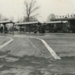 Fotografia przedstawia teren dworca autobusowego. Widoczne zadaszone wiaty oraz flagi państwowe zamocowane na słupach.