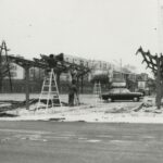 Fotografia przedstawia szkielety stawianych wiat autobusowych. Widoczni robotnicy montujący konstrukcje - z drabinami. Z tyłu bloki.