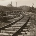 Fotografia przedstawia fragment torów. W tle widoczne pagórki kamieniołomu. Wzdłuż torów sprzęt.