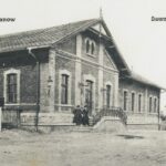 Fotografia przedstawia dwóch mężczyzn przed ceglanym budynkiem stacji kolejowej w Chrzanowie.