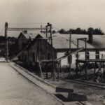 Fotografia przedstawia teren zakładu wydobywczego: zabudowania, rusztowania, rury.