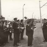 Fotografia przedstawia orkiestrę z dyrygentem na peronie stacji kolejowej. W tle widoczna tablica „Chrzanów-Śródmieście”.