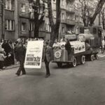 Fotografia mężczyzn niosących tablicę „Wydział Montażu Lokomotyw”. Za nimi pojazd z logo W-4 oraz napisem „Złoty Jubileusz 50”.