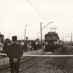 Fotografia przedstawia ludzi na peronie, którzy obserwują wjazd pociągu na stację. W tle widoczne flagi narodowe, tablica „Chrzanów-Śródmieście”, napis „peron 2”.