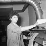 Fotografia przedstawia kobietę przytrzymującą płat papieru przechodzący pod rolką w maszynie kopiującej.