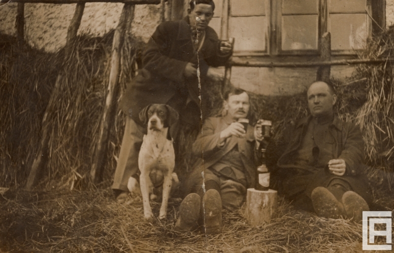 Fotografia przedstawia trzech mężczyzn na sianie popijających piwo ze szklanek. Obok siedzi pies.