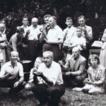 Fotografia przedstawia kilkanaście osób stojących lub kucających, które dzidkami jedzą pieczone.