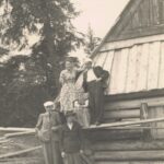 Fotografia przedstawia grupę pięciu osób: dwóch kobiet i trzech mężczyzn przed drewnianym domem.