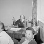 Fotografia przedstawia mężczyznę siedzącego za biurkiem. Naprzeciw niego, ale zwrócone do aparatu, siedzą trzy kobiety.
