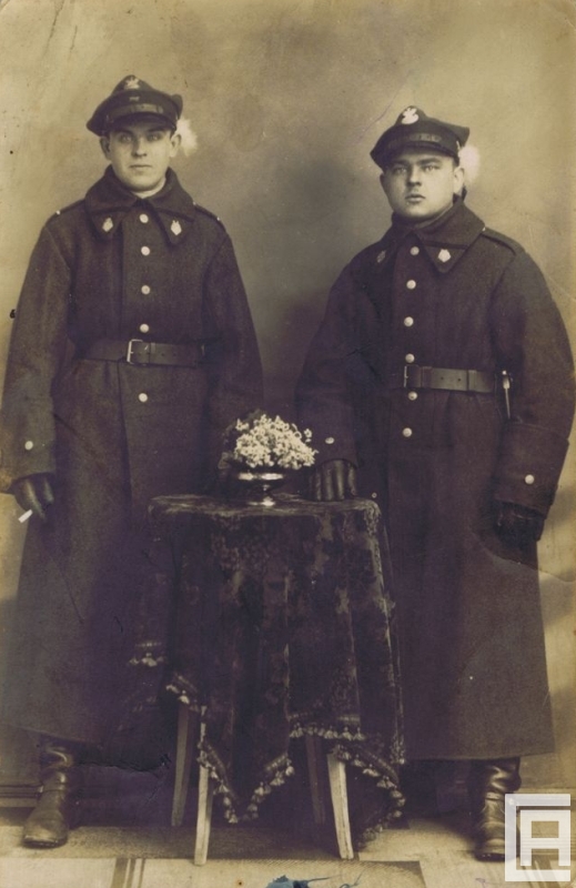Fotografia przedstawia dwóch mężczyzn w mundurach pozujących do obiektywu w studio fotograficznym.