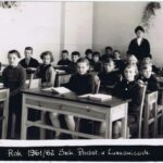 Fotografia przedstawia dwa rzędy ławek szkolnych z uczniami. Z tyłu widoczna nauczycielka.