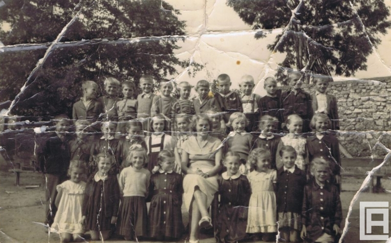 Fotografia przedstawia trzy rzędy uczniów i nauczycielkę pozujących do zdjęcia. Widoczne liczne uszkodzenia odbitki.