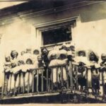 Fotografia przedstawia grupę dzieci i nauczycielek stojących na balkonie budynku. Uczniowie mają przebrania.