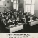 Fotografia przedstawia dwa rzędy ławek szkolnych z uczniami. Z tyłu nauczycielka. Po prawej tablica z napisem „Szkolne Koło PCK” oraz fragment ściennej mapy Polski.