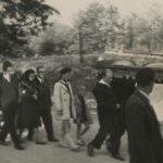 Fotografia przedstawia kolumnę ludzi odprowadzających trumnę podczas ceremonii pogrzebowej.