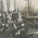 Fotografia przedstawia trzy kobiety i dwóch chłopców na cmentarzu. Grób, przy którym stoją, jest świeżo przykryty wieńcami pogrzebowymi, nie ma jeszcze tablicy nagrobkowej.