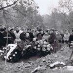 Fotografia przedstawia grupę ludzi – mężczyzn, kobiet i dzieci stojących nad świeżo zasypanym grobem.