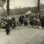 Fotografia przedstawia tłum ludzi odprowadzających trumnę podczas ceremonii pogrzebowej.