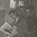 Fotografia przedstawia mężczyznę przeglądającego gazetę obok choinki bożonarodzeniowej.