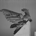 Fotografia przedstawia zbliżenie rzeźby orła na pomniku, podświetlenie.