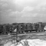 Fotografia przedstawia plac budowy naprzeciw bloku mieszkalnego. Z lewej strony widoczny cokół przyszłego pomnika z rusztowaniem.