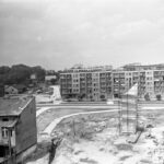 Fotografia przedstawia plac budowy naprzeciw bloku mieszkalnego. Z prawej strony widoczny cokół przyszłego pomnika z rusztowaniem.
